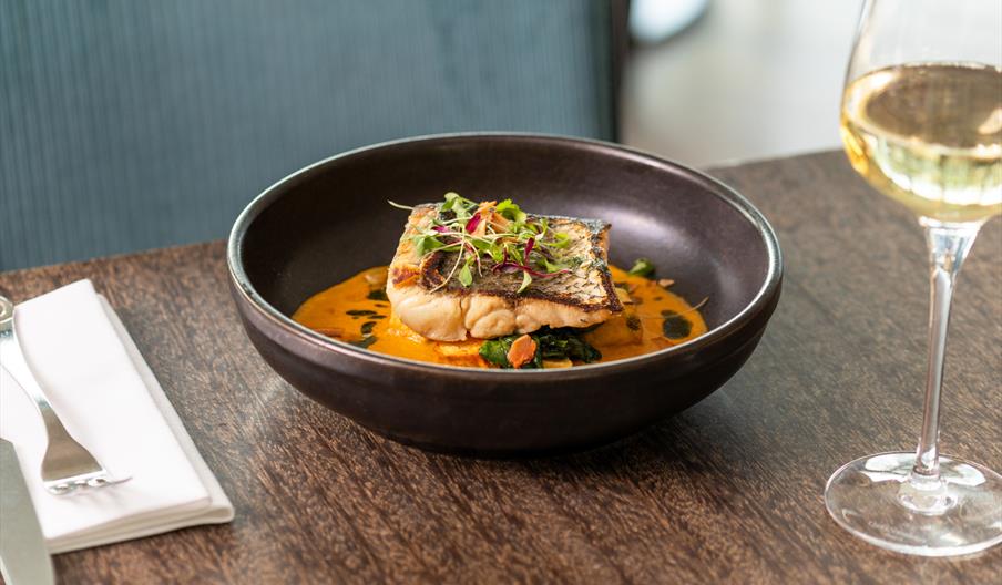 Fish dish served with sauce and a glass of white wine.
