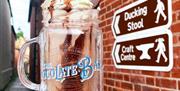 A delicious looking milkshake held aloft next to a brick wall with a brown information sign that points towards the ducking stool.