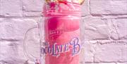 A vibrant pink jammy-dodger flavoured milkshake held infront of an equally bright pink brick wall.