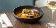 Fish dish served with sauce and a glass of white wine.