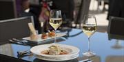 Dining table set with two glasses of white wine and plated dishes.