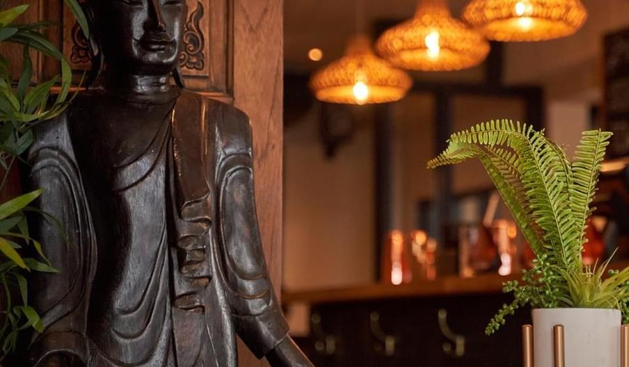 Nusara Thai restaurant with a thai statue and warm lighting and plants Nusara Thai restaurant with a thai statue and warm lighting and plants